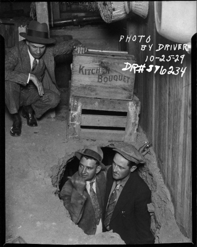 Драйвер.
Бутлегерский рейд. 3 детектива во время рейда против нелегальных торговцев алкоголем, двое вылезают из дыры в земле. 
25.10.1929.
Серебряно-желатиновый отпечаток.
Предоставлено Фототекой Лос-Анджелеса