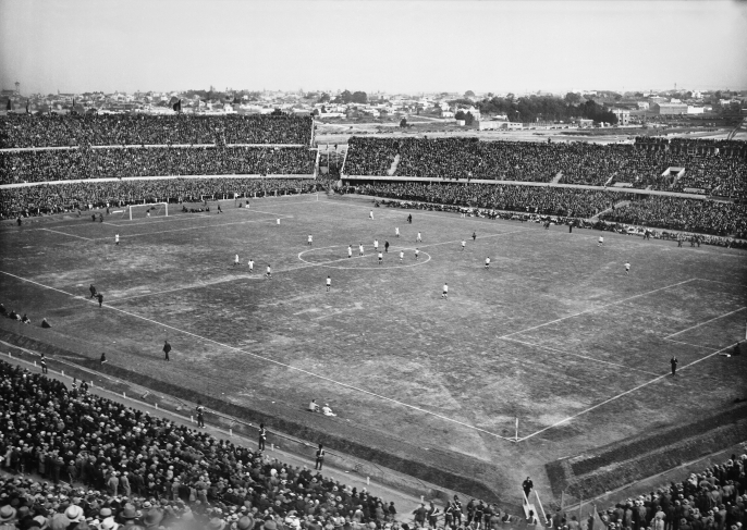 Матч между Уругваем и Перу, в день открытия Стадиона Сентенарио. Впереди слева: Олимпийская трибуна. Справа: Трибуна Коломбес. На заднем плане слева: Трибуна Амстердам; справа: Трибуна Америка.
18 июля 1930 года.